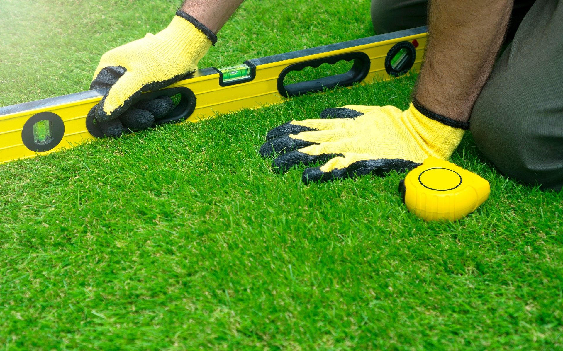Worker doing the artificial grass installation and checking tilt with the level